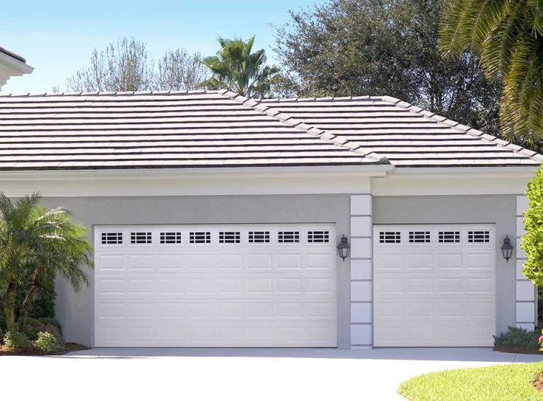 Two white garage doors on a light gray house with a tiled roof.