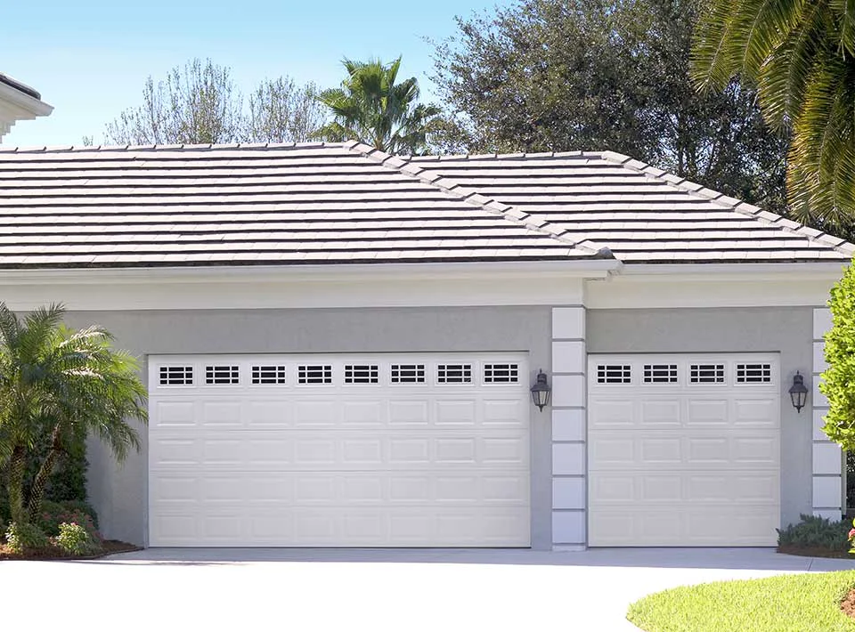 Two white garage doors on a light gray house with a tiled roof.