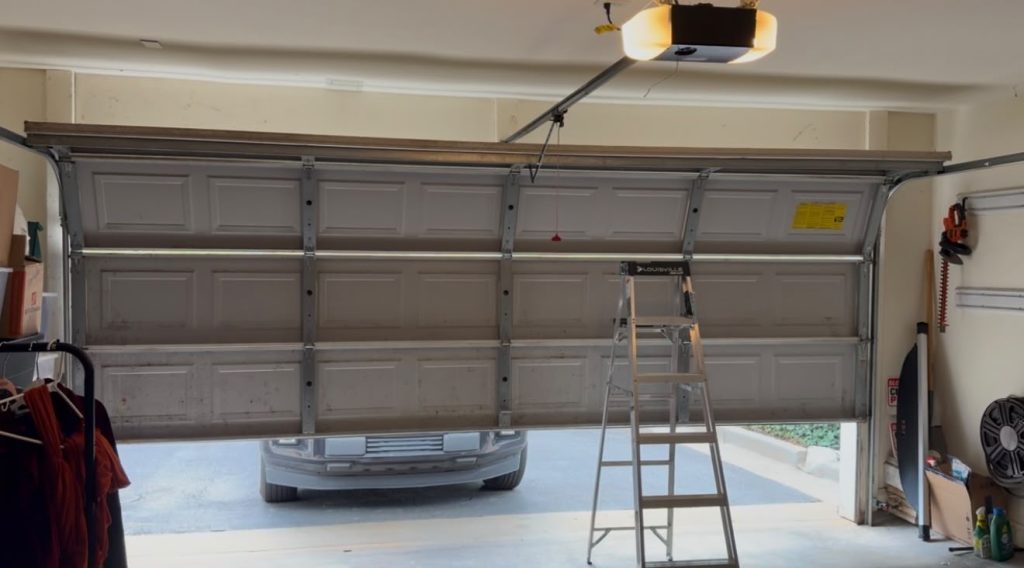 Garage door partially open with a ladder and car visible