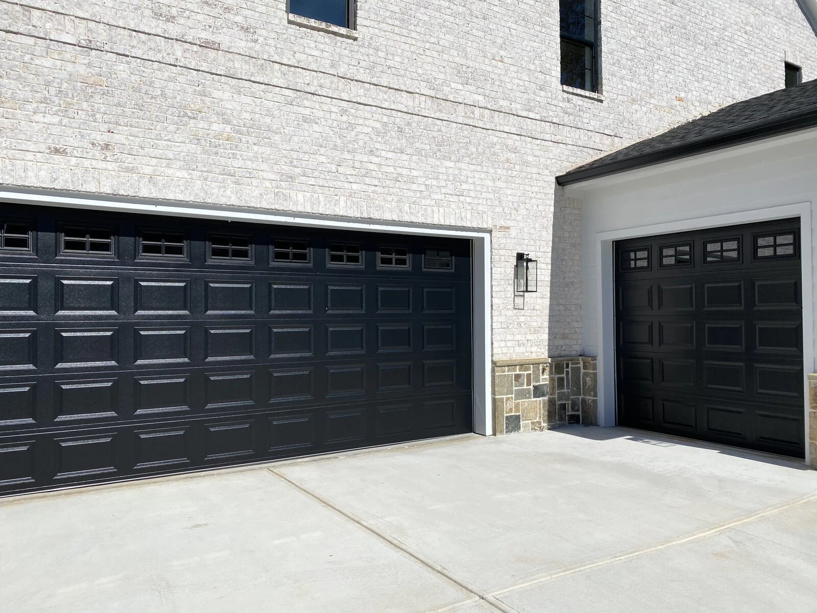 Two dark garage doors on a white brick house with a concrete driveway.