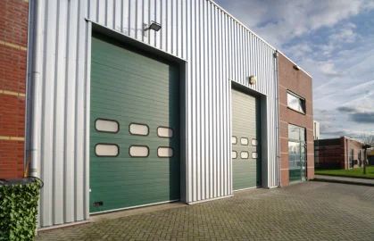 Two green garage doors on a metal building with brick accents.