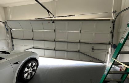 White garage door partially open with a white car and green ladder