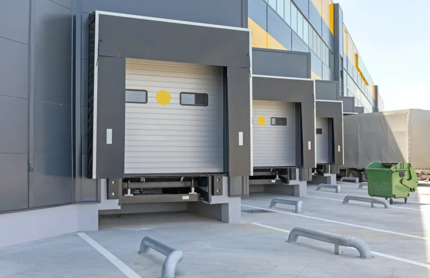 Loading docks with closed doors and a green dumpster outside a warehouse.